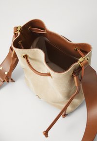 Borsa a secchiello in suede beige con tracolla in pelle marrone, dettagli in metallo dorato, chiusura con coulisse e fodera interna liscia.