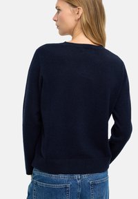 Granatowy sweter dzianinowy o luźnym kroju, okrągłym dekolcie i ściągaczu na dole. Materiał wydaje się miękki w dotyku, o gładkiej fakturze, bez widocznych wzorów.