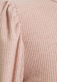 Weicher rosa gerippter Stoff mit vertikalen Linien, der eine subtile Textur und ein leicht zerknittertes Erscheinungsbild aufweist, was das gemütliche Design unterstreicht.
