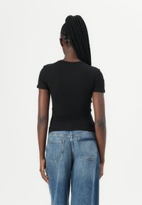 Black short-sleeve t-shirt viewed from the back, fitted design, lightweight fabric, paired with light blue wide-leg jeans.