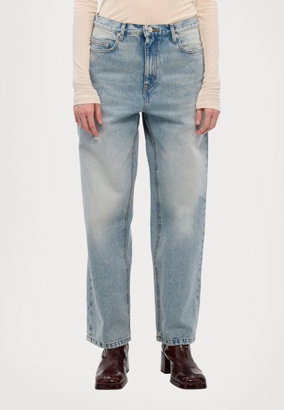 Light blue denim wide-leg jeans with five pockets, faded sections, and exposed stitching. Paired with brown heeled boots.