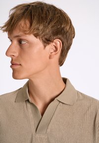 Polo shirt beige a coste con colletto e una superficie leggermente texture. Design semplice, forma aderente e delicati dettagli di cucitura.