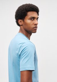 Hele sinine puuvillane lühikeste varrukatega T-särk, ümmarguse kaelusega ja siledat tekstuuri, kujutatud inimesel küljelt vaates.