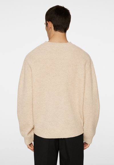 Beige kötött pulóver laza szabással, bordázott textúrával, széles ujjakkal és kerek nyakkivágással, egyenes hátrésszel.