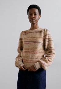 Strikkegenser i beige med flerfargede horisontale striper. Har rund hals og ribbede mansjetter. Myk tekstur og løs passform.