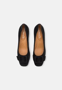 Ballerines en daim noir avec un bout carré et une boucle décorative à l'avant. L'intérieur présente une doublure beige clair et une semelle intérieure rembourrée.