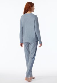 Blusa de manga larga azul clara y pantalones a juego en tejido suave. La blusa presenta un escote redondo; los pantalones tienen detalles acanalados en los laterales y puños.