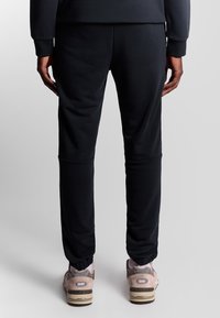 Zwarte sportbroek met een slim fit, voorzien van elastische boorden bij de enkels en een gladde, rekbare stof. Draag het met lichte sneakers.