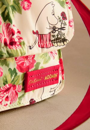 Stofftasche mit Blumenmuster und roten Akzenten, die eine Moomin-Figur in einem Blumengarten zeigt. Auf einer Seite befindet sich ein Markenlabel.