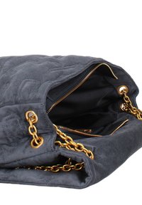 Sac à main en daim gris avec des anses en chaîne dorée, présentant un compartiment zippé et un motif de surface texturé. L'intérieur est doublé de noir.