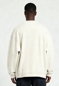 Vue arrière d'une personne portant un sweat-shirt oversize écru et un pantalon cargo noir sur un fond uni.