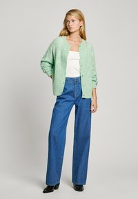 Miņu zaļš adīts kardigāns ar brīvu piegriezumu, pogu aizdari un ribotām piedurknēm, apvienots ar augstās jostas vietas zilo denim plašo biksēm un melniem papēžiem.