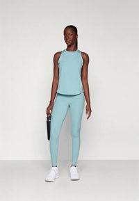 Canotta sportiva azzurro chiaro e leggings, entrambi realizzati in tessuto liscio ed elastico. La modella tiene in mano una borraccia nera. Scarpe da ginnastica bianche completano il look.