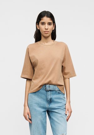 T-shirt en coton marron à manches courtes, col rond, coupe décontractée. Associé à un jean en denim bleu clair avec une taille ceinturée et une coupe droite.