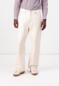 Hvide denim bukser med en afslappet pasform, der har baglommer, lukning med knap og kontrastsyede detaljer. Stylisteret med hvide sneakers.
