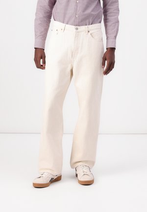 White denim pants with a relaxed fit, featuring back pockets, a button closure, and contrasting stitching details. Styled with white sneakers.