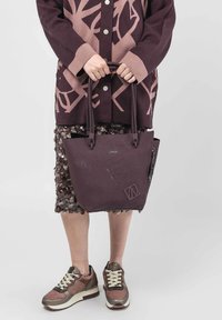 Bolso tote de color púrpura intenso con una superficie texturizada y patrones grabados, que cuenta con asas dobles y un diseño elegante y minimalista.
