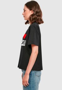 T-shirt en coton noir avec des manches courtes et une coupe décontractée, portant l'inscription "J'adore la pizza" en lettres rouges et blanches.