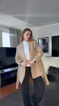 Beżowa oversize marynarka z kołnierzem typu szal, zapinana na guziki, o dopasowanym kroju, zestawiona z białym topem i czarnymi szerokimi spodniami.