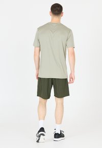 Lichtgrijze t-shirt met korte mouwen en donkergroene shorts, gemaakt van zachte stof. Heeft een relaxte pasvorm en minimalistisch ontwerp. Zwarte sportschoenen.
