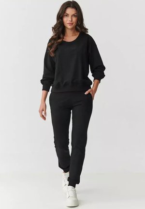 Czarny sweatshirt oraz dopasowane dresy wykonane z miękkiego materiału, z luźnym krojem, ściągaczami na mankietach i kieszeniami bocznymi. Białe sneakersy dopełniają stylizację.