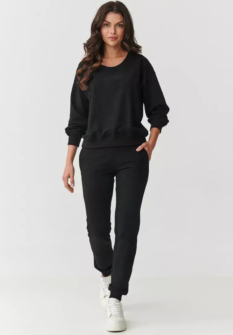 Czarny sweatshirt oraz dopasowane dresy wykonane z miękkiego materiału, z luźnym krojem, ściągaczami na mankietach i kieszeniami bocznymi. Białe sneakersy dopełniają stylizację.