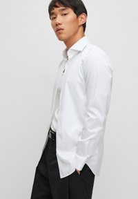 Camisa blanca de manga larga hecha de tela suave, con cuello de solapa, un placket de botones y un corte ajustado, combinada con pantalones negros.