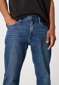 Jeans de mezclilla azul con un diseño de pierna recta, estilo de cinco bolsillos, un sutil desgastado y un cierre de botón de metal en la cintura.