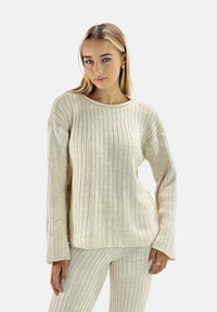 Beżowy sweter prążkowany z długimi rękawami, okrągłym dekoltem i teksturowanym materiałem. Połączony z dopasowanymi prążkowanymi spodniami dzianinowymi.