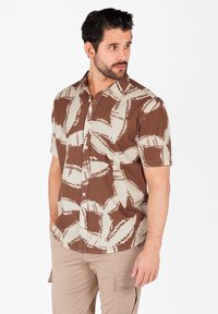 Camicetta corta marrone e beige con un motivo a foglie, chiusura a bottoni, e tessuto testurizzato con una vestibilità comoda.