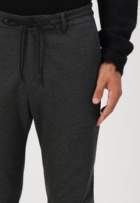 Mørkegrå sweatpants med snøring i livet, glat tekstur og afslappet pasform. Synlige syninger og lomme detaljer forbedrer designet.