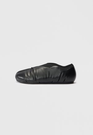 Black slip-on shoe with smooth leather material, rounded toe, stretchy opening, and minimal branding detail on the side.