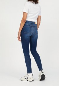 Džíny s vysokým pasem v modré barvě vyrobené z denimové látky, s přiléhavým střihem, pěti kapsami a decentními švy, doplněné bílými teniskami.