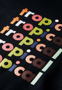 Palabra repetida "tropical" en letras negritas y coloridas dispuestas en diagonal sobre un fondo de tela negra.