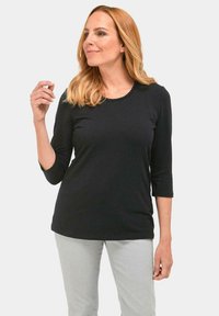 Zwarte, lange mouwen top met een ronde halslijn en decoratieve stiksel. Gecombineerd met lichtgrijze broek, met een eenvoudig en aansluitend ontwerp.