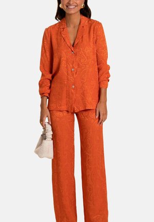 Camisa de botones de manga larga con un estampado de paisley naranja y pantalones de pierna ancha a juego, complementados por un pequeño bolso de color crema.