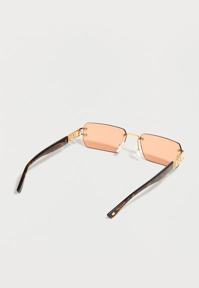 Ορθογώνια γυαλιά ηλίου με ροζ φακούς, χρυσή μεταλλική γέφυρα και αρθρώσεις, και μπράτσα με σχέδιο χελώνας σε ανοιχτό φόντο.