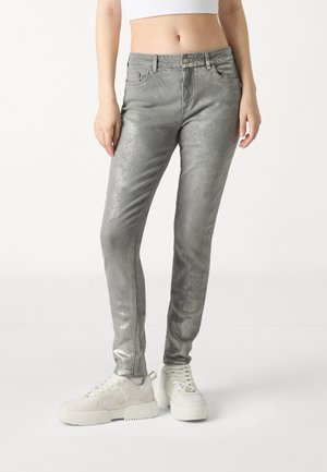 Strieborné metalické skinny džínsy s hladkou textúrou, dizajnom s piatimi vreckami a stredne vysokým pásom. V kombinácii s bielymi robustnými teniskami.