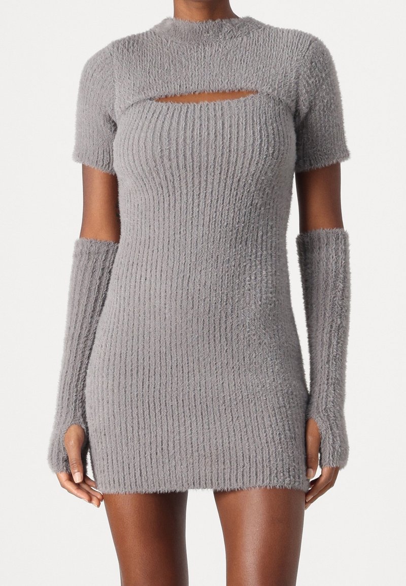 Femme portant une mini-robe en maille grise duveteuse avec manches courtes, une découpe poitrine et des longs gants sans doigts assortis.