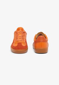 Baskets en cuir et daim orange avec une finition texturée, dotées de lacets plats, d'une semelle en caoutchouc et d'un logo de marque embossé sur le talon.