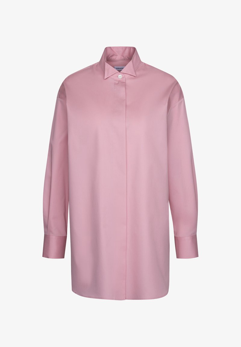 Chemise rose à manches longues, coupe ample, avec col pointu et un seul bouton blanc visible en haut.