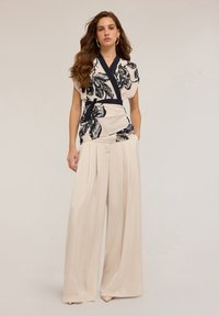 Blouse en soie à motif floral avec des accents bleu marine, accompagnée de pantalons beiges à jambes larges avec des plis avant et une texture lisse.