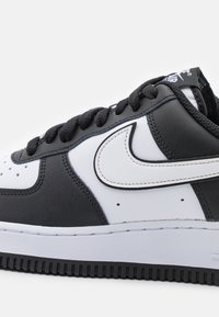 Black and white Nike Air Force 1 sneaker with black laces, white swoosh logo, and textured black sole on a white background.