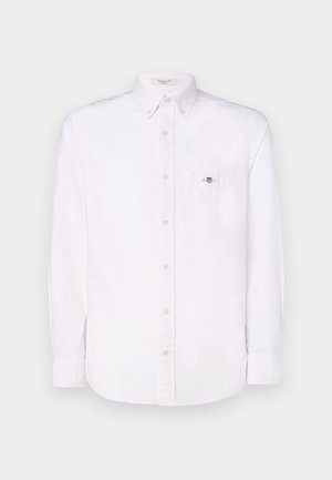 Camicia bianca a maniche lunghe con bottoni, caratterizzata da un sottile motivo a righe verticali, dotata di una tasca sul petto e di un piccolo emblema sulla tasca.