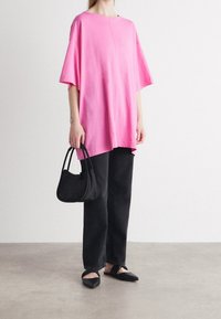 Camiseta de algodón rosa de gran tamaño con cuello redondo, combinada con pantalones de mezclilla negros y zapatos planos negros. Lleva un bolso negro de hombro.