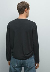 Sort langærmet skjorte med en afslappet pasform, glat tekstur, rund halsudskæring og sænket skuldre, parret med mid-blå denim jeans.