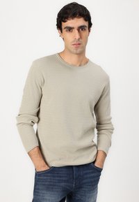 Suéter de canalé gris claro con cuello redondo y mangas largas, combinado con jeans azul oscuro. La tela tiene un aspecto texturizado.