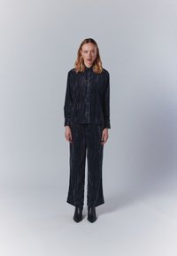 Tengerészkék, gyűrött anyagból készült két részes öltözet, amely egy galléros, gombos ingből és hozzá illő, bő szárú nadrágból áll. Fekete bokacsizmák.