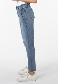 Helle blaue High-Waist-Jeans mit einem gerafften Elastikbund, geraden Beinen und einer einzigen Gesäßtasche, kombiniert mit weißen Sneakers.