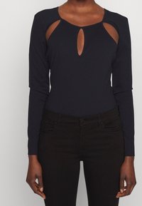 Svart långärmad topp med utskärningar på axlarna och en nyckelhalsringning. Tillverkad av ett mjukt material, kombinerad med mörka jeans.